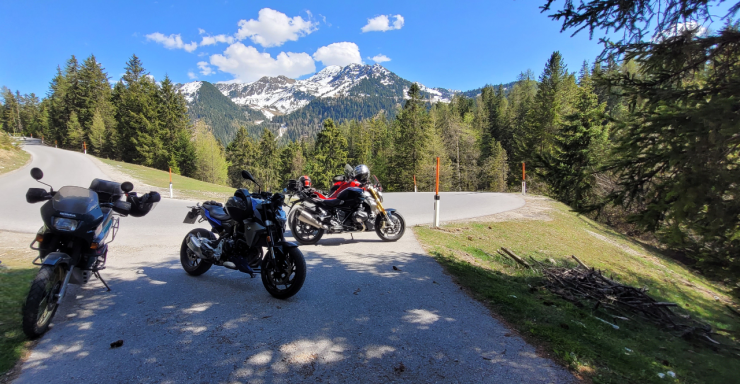 Drei Motorräder auf einem klaren Weg mit Bergen im Hintergrund und Bäumen.