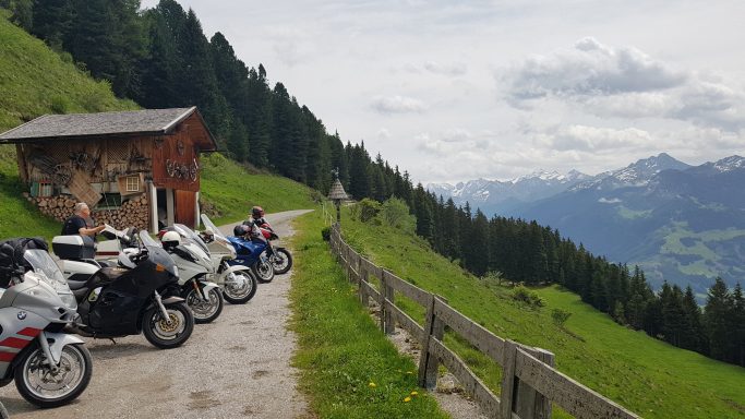 Motorräder stehen an einem schmalen Weg mit Berglandschaft im Hintergrund.