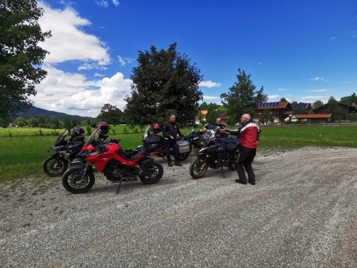 Gruppe von Motorrädern und Fahrern auf einem Schotterplatz vor schöner Landschaft.