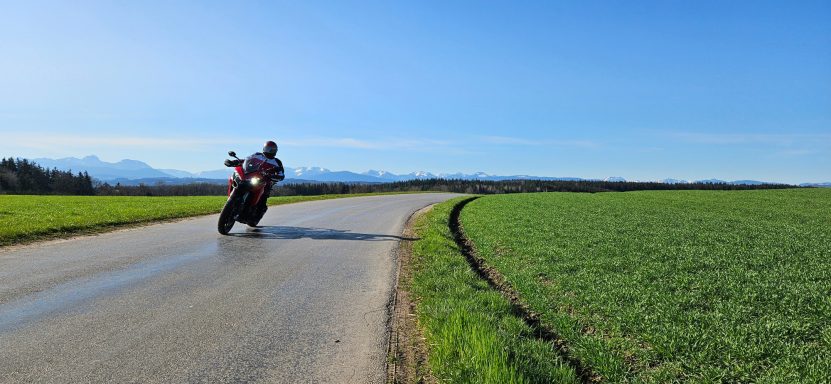 Motorradfahrer auf einer kurvigen Landstraße neben einem grünen Feld.
