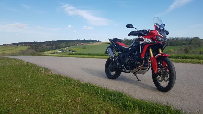 Motorrad auf einer kurvenreichen Straße mit grünen Hügeln im Hintergrund.